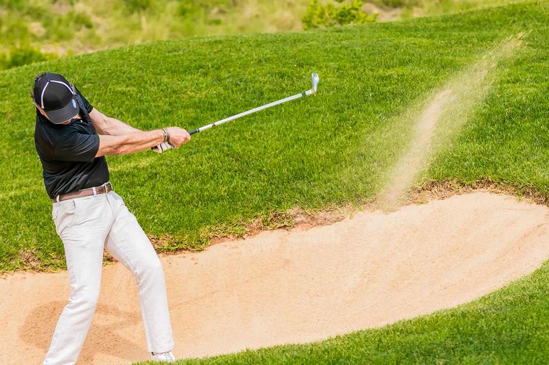 Ein Golfer schießt aus dem Sand seinen Ball zurück ins grün