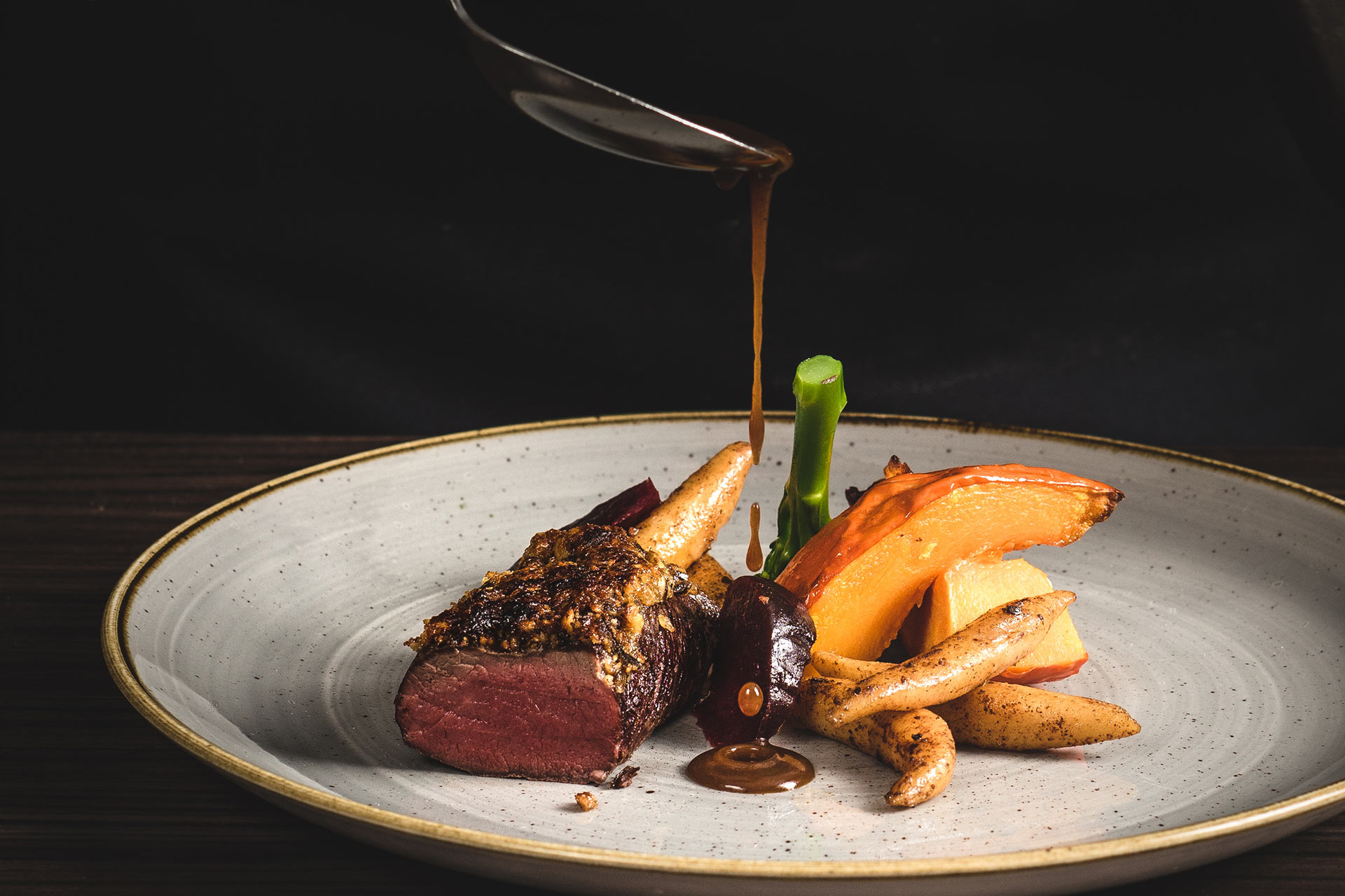 Ein Koch gießt Sauce mit einem Löffel über ein Gericht aus Fleisch und Gemüse