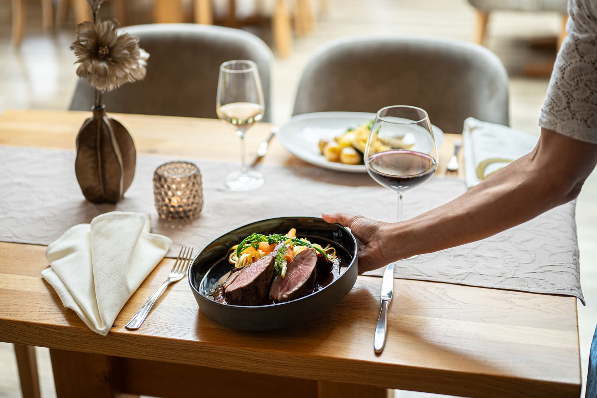 Eine Kellnerin serviert eine Hauptspeise an einen eingedeckten Tisch im Restaurant